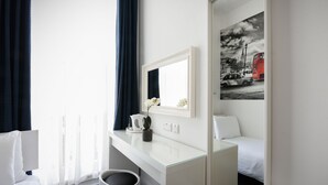A hotel room with a white bed, a white desk, a potted plant, a mirror, and a painting of a red bus. - Meridiana (London)