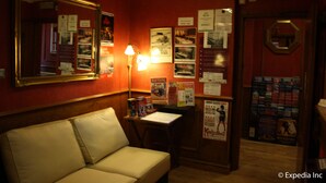 A hotel room with a sofa, a desk with a lamp, and a bulletin board with various notices and posters. - Meridiana (London)