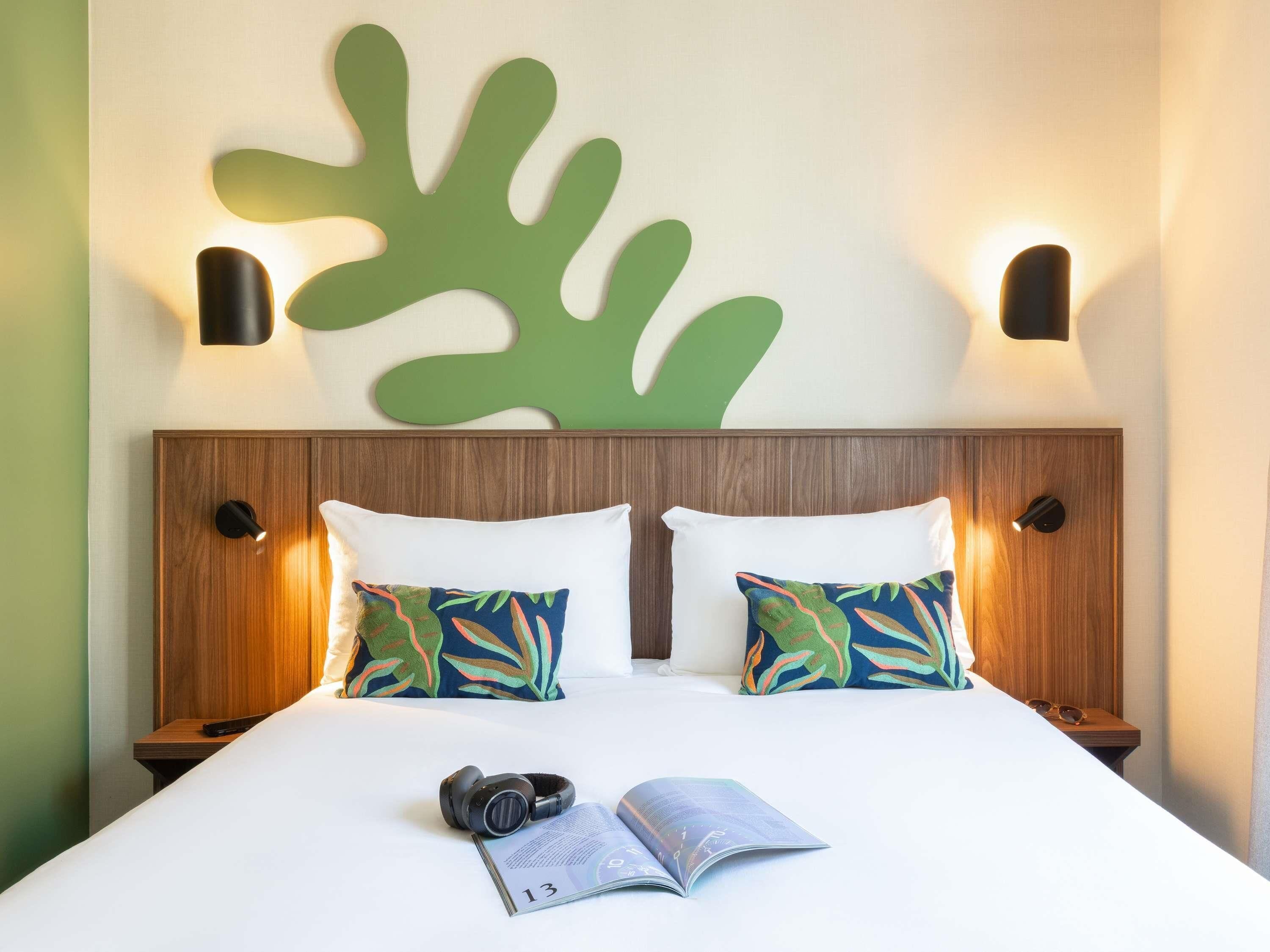 A neatly made bed with two pillows, a pair of headphones, and an open magazine on a white bedspread.