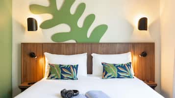 A neatly made bed with two pillows, a pair of headphones, and an open magazine on a white bedspread.
