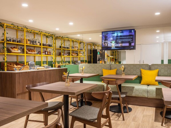 A cafe interior with wooden tables, green cushioned seating, and shelves stocked with jars and baskets. - ibis Styles Paris Jardin de la Villette (Paris)