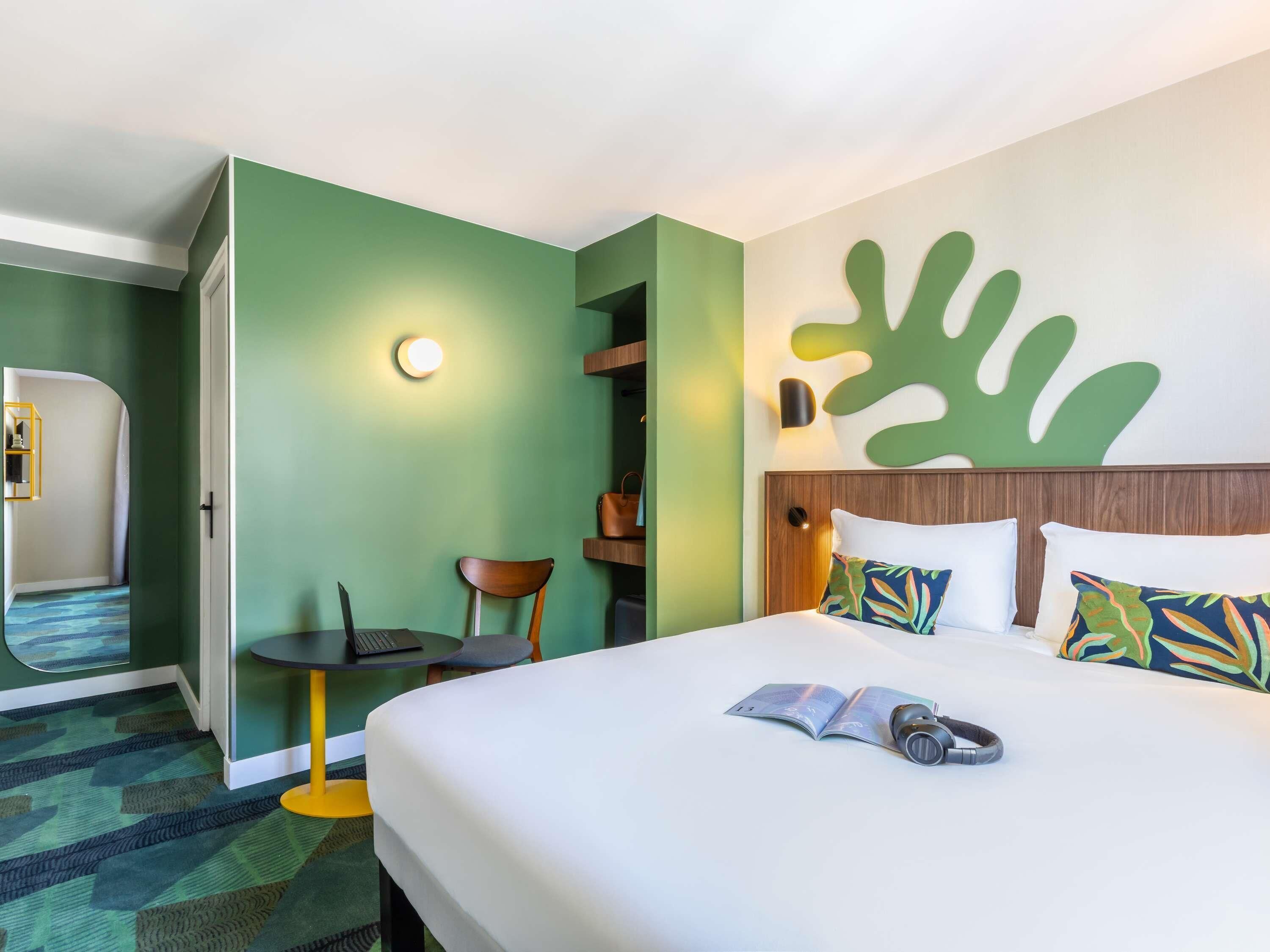 A hotel room with a bed, a desk, a chair, and a wall-mounted shelf.