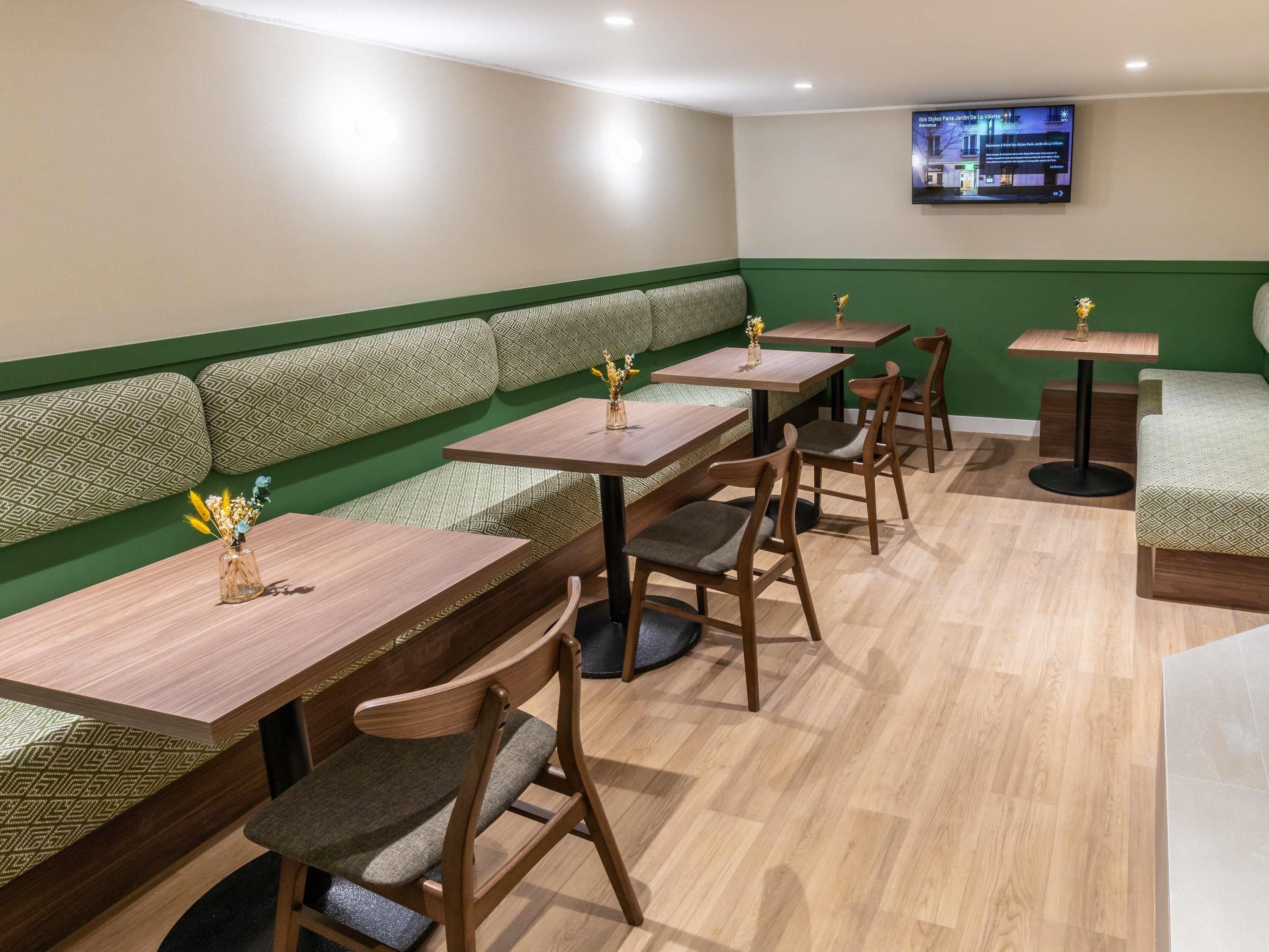 Een restaurantinterieur met groene gestoffeerde zithoeken, houten tafels en stoelen.