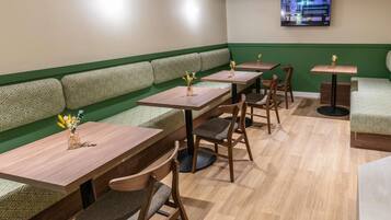 Een restaurantinterieur met groene gestoffeerde zithoeken, houten tafels en stoelen.