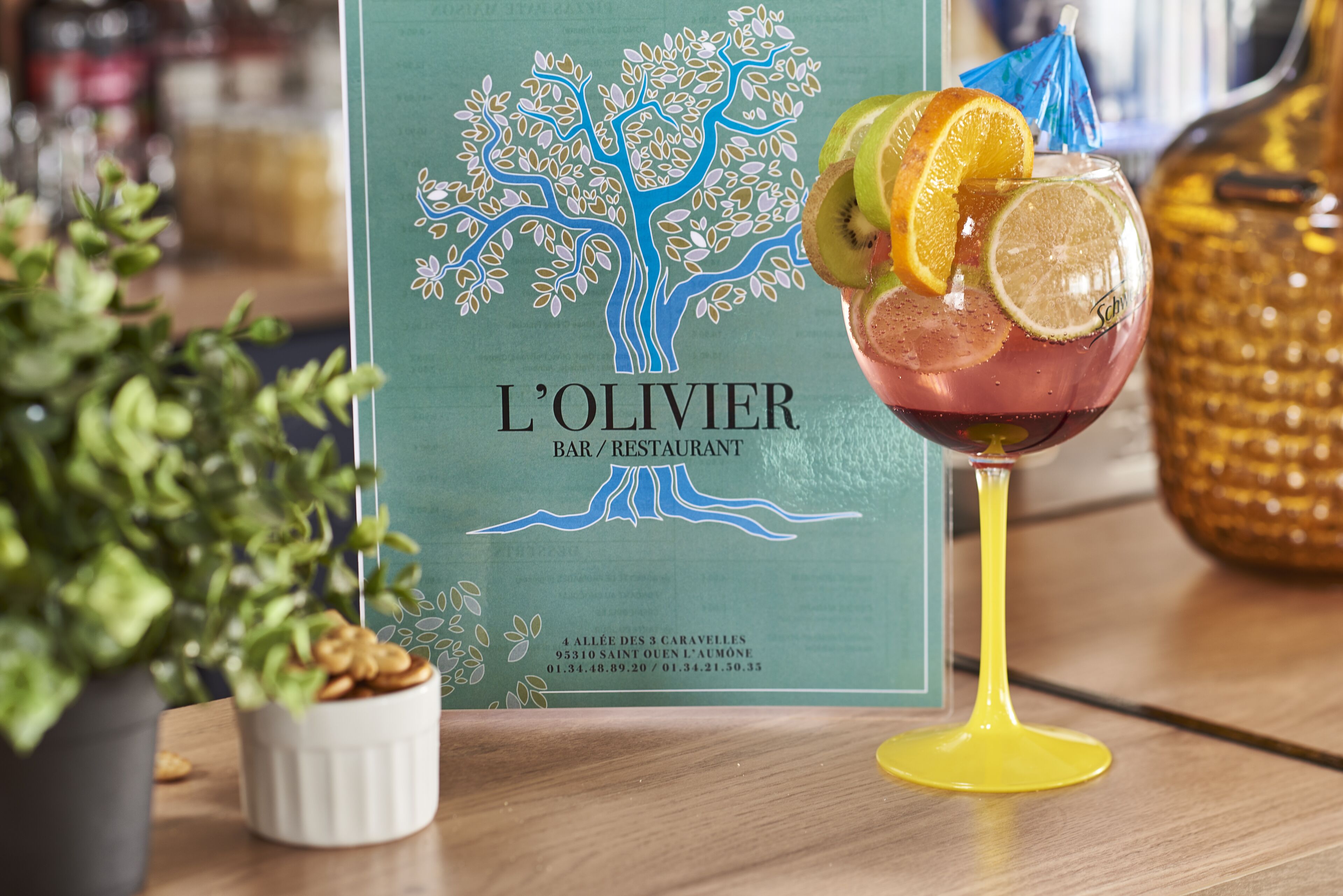 A menu from L'Olivier Bar/Restaurant with a tree design, a glass of drink with fruit slices, and a potted plant.