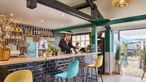 A bar area with a bartender, a brick counter, and bar stools. - ibis budget Saint Ouen l'Aumône (Saint-Ouen-l'Aumone)
