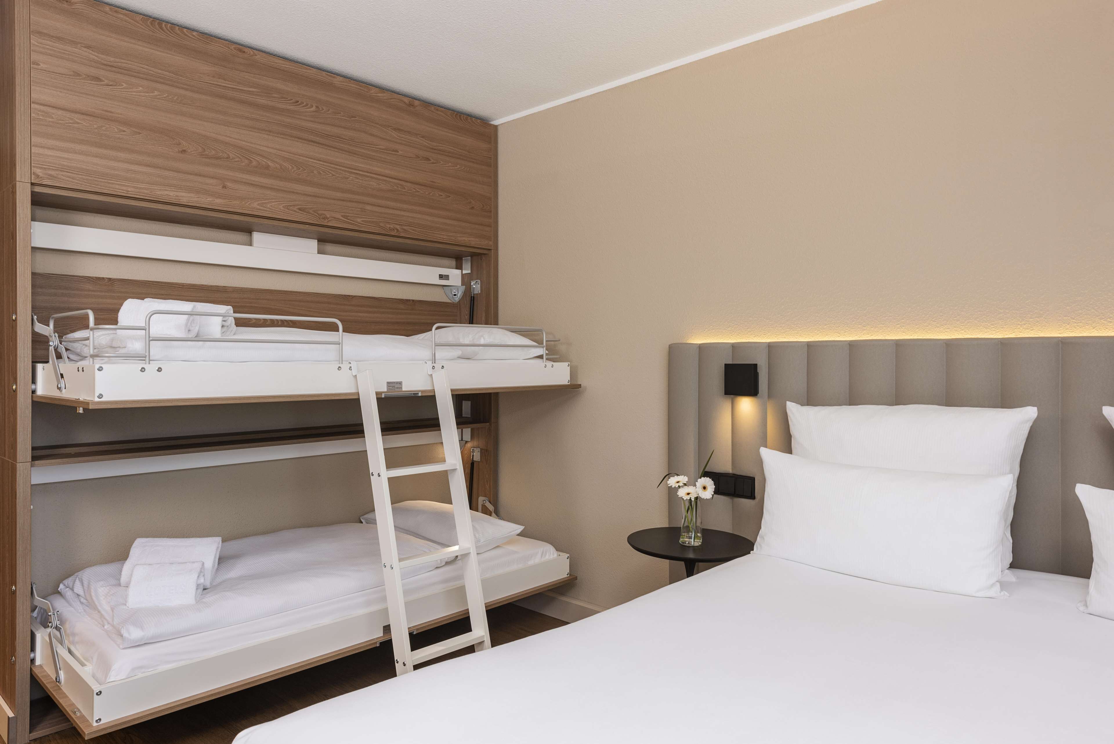 Une chambre avec un lit superposé doté d’une tête de lit en bois, une table de chevet avec une lampe et un vase rempli de fleurs.