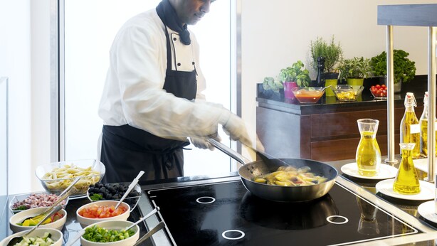 Un cocinero preparando comida en una estufa, rodeado de ingredientes y condimentos.