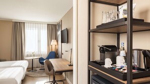 Una habitación de hotel con cama, escritorio, silla, televisor y minibar.