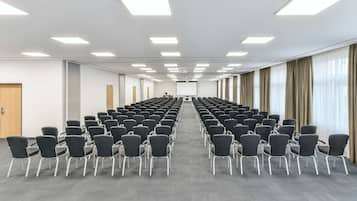 A conference room with rows of chairs, a projector screen, and a large window with curtains.