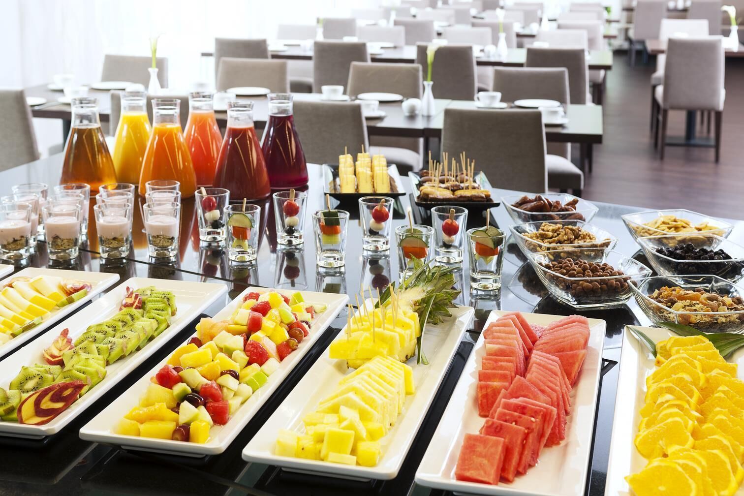 Una mesa de buffet con frutas, jugos y postres varios.