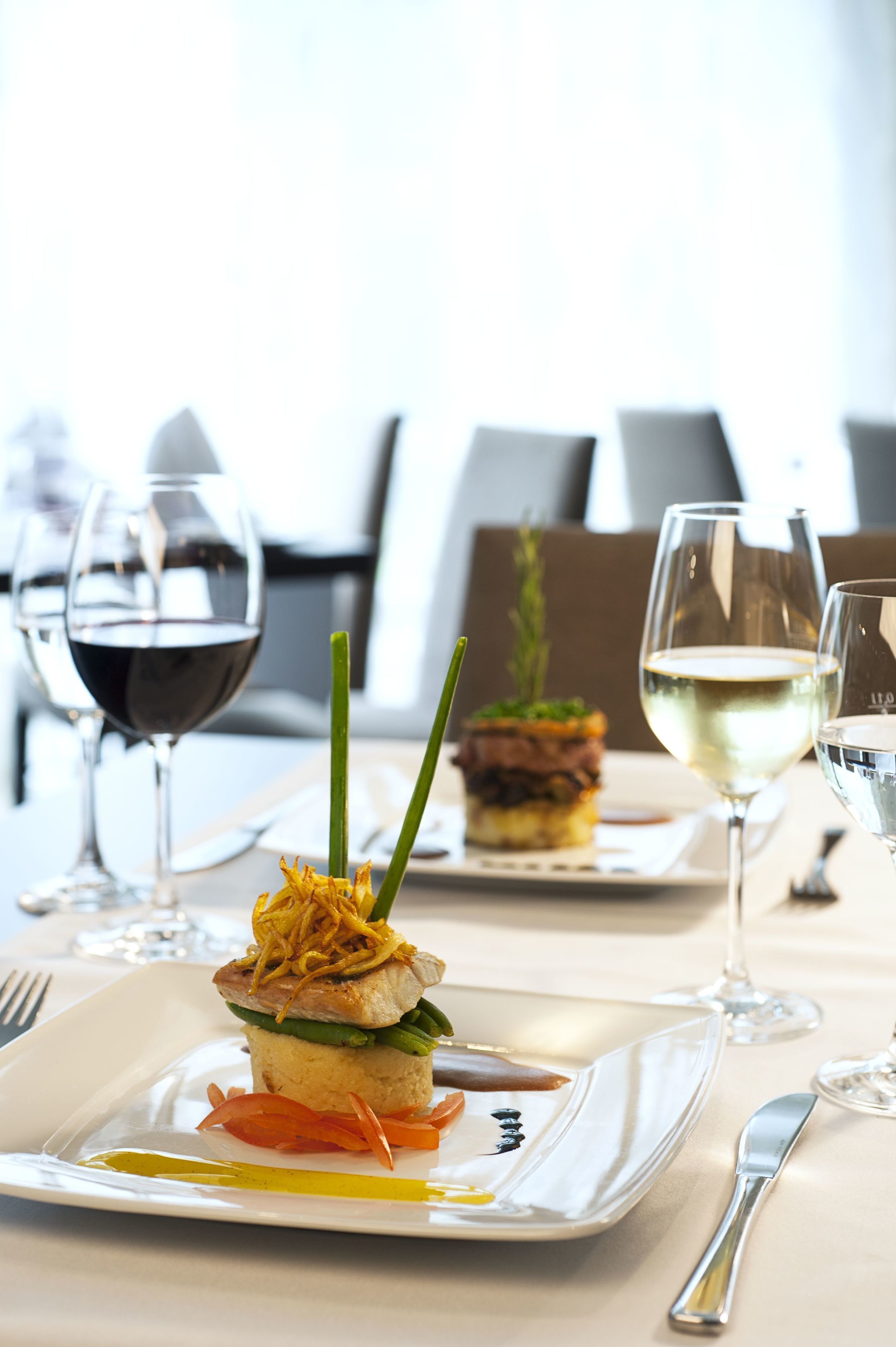 Una mesa de comedor con una comida dispuesta con esmero, que incluye un sándwich y una copa de vino blanco.
