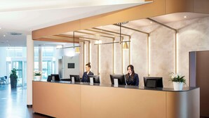 Un mostrador de recepción con tres empleados, un interior moderno con suelo de madera y ventanas amplias que dejan entrar luz natural.