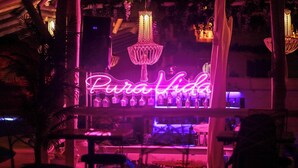 Zona de bar con un letrero de neón que dice 'Pura Vida' y candelabros de cristal colgantes.