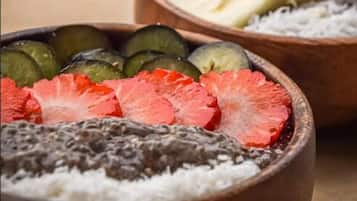 Three wooden bowls filled with sliced fruits and a white substance, likely coconut, on a table near a pool.