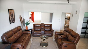 Una sala de estar con dos sofás de cuero marrón, una mesa de centro y un ventanal con cortinas.