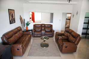 A living room with two brown leather sofas, a central coffee table, and a large window with curtains.