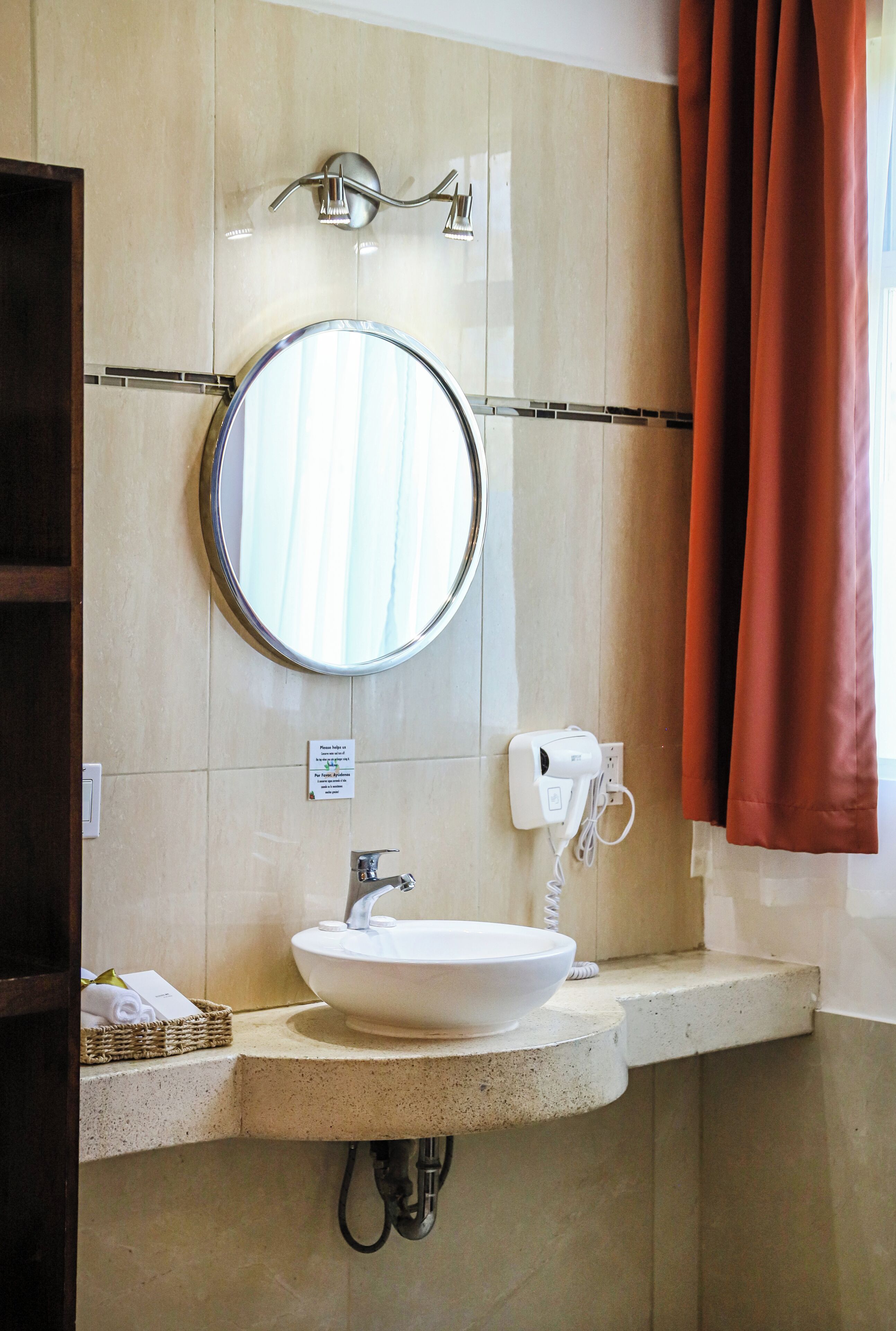 A bathroom with a round mirror, a white sink, a towel basket, and a shower curtain.