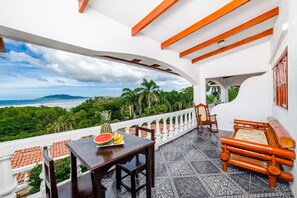 Enjoy the ocean view from this balcony with a table, bench, and fruit bowl.