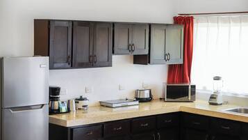 Una cucina con mobili scuri, un frigorifero, un forno a microonde, un tostapane e un frullatore sul piano di lavoro.