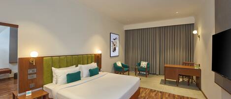 Una habitación de hotel con una cama grande, un escritorio, una silla, un televisor y una ventana con cortinas.