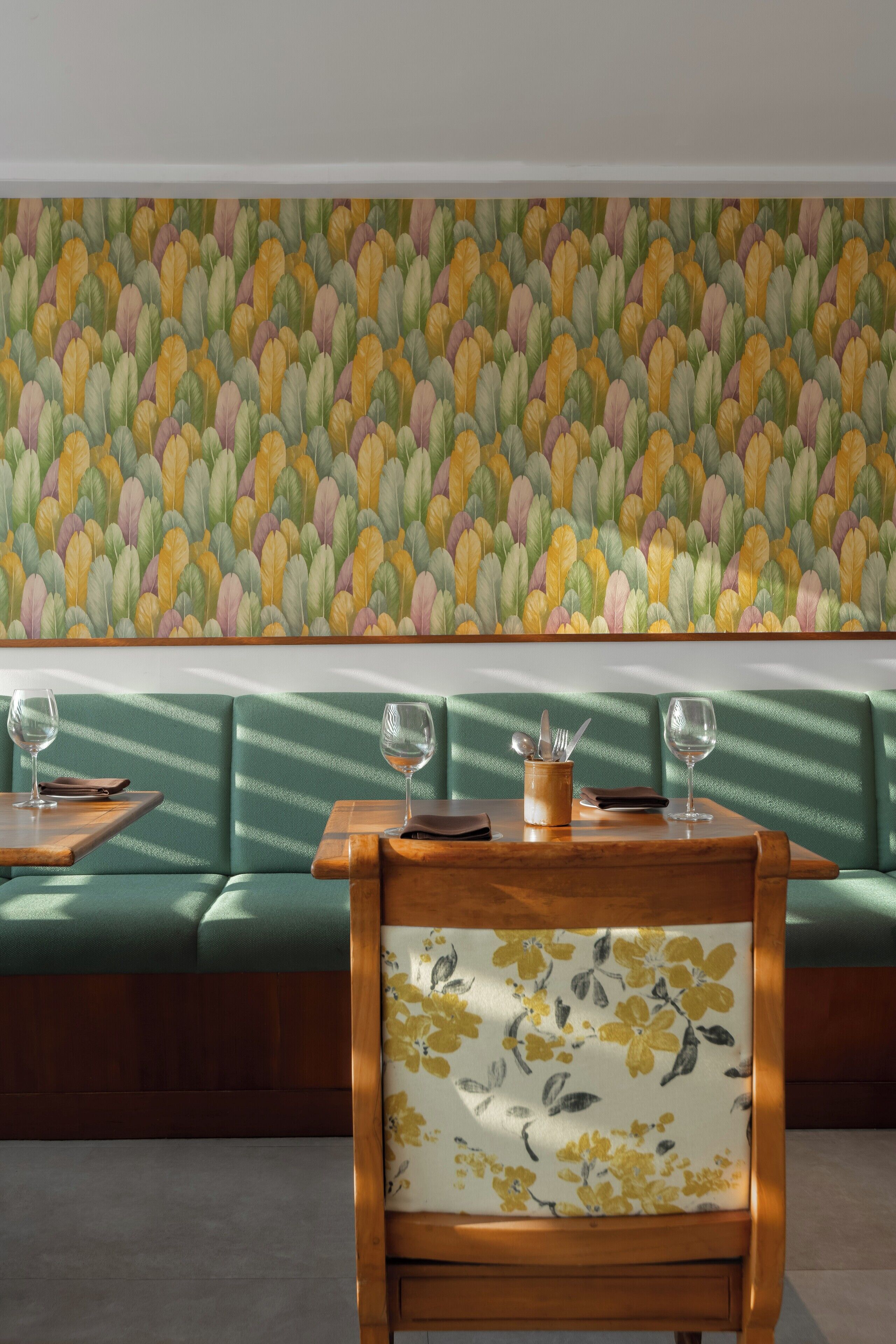 A restaurant interior with green upholstered seating, wooden tables, and a floral-patterned chair.