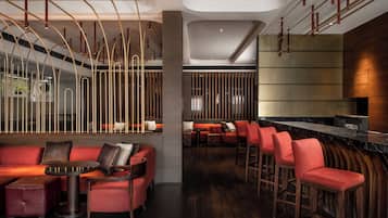 Een moderne bar met rode zitplaatsen, een gebogen toog en een hoge plafond met unieke verlichtingsarmaturen.