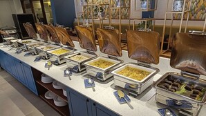 A buffet setup with various food items and utensils. - The Avenue Regent (Kanayannur)