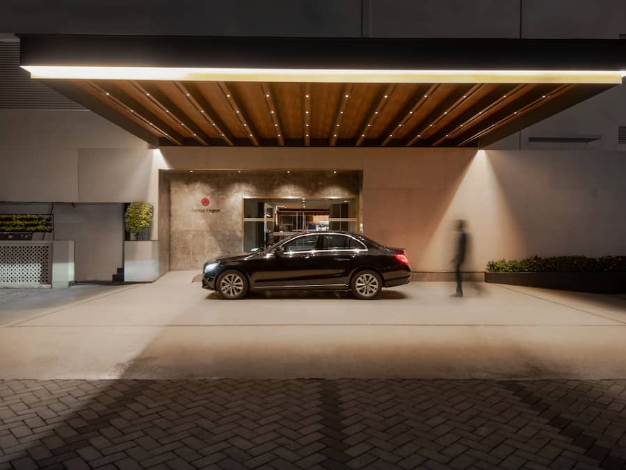 Una entrada moderna de edificio con un coche negro estacionado adelante, techo de madera y un letrero que dice "Avenue Elegance".