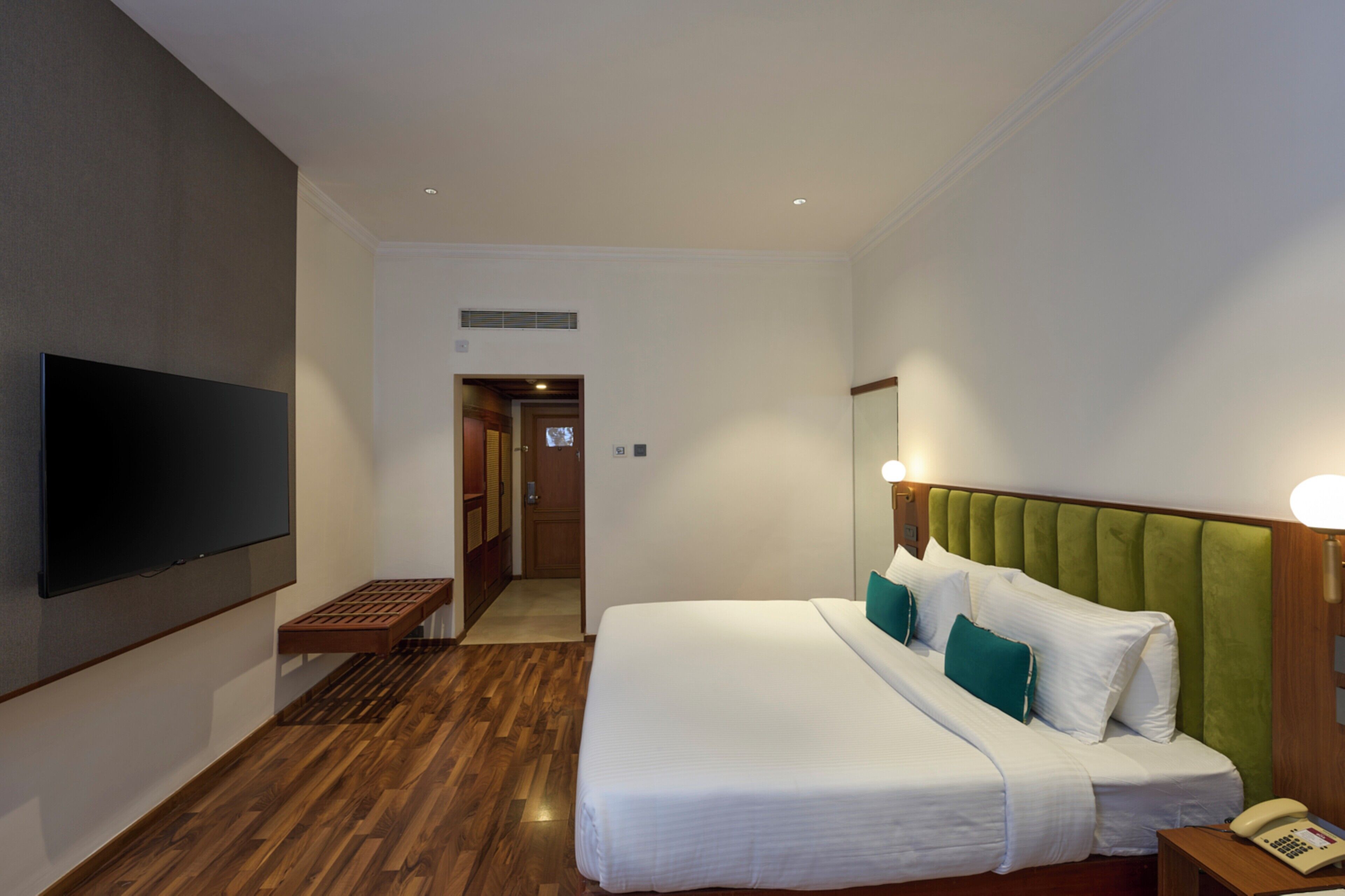 Una habitación de hotel con una cama grande, un televisor de pantalla plana en la pared, un teléfono en la mesita de noche y suelo de madera.
