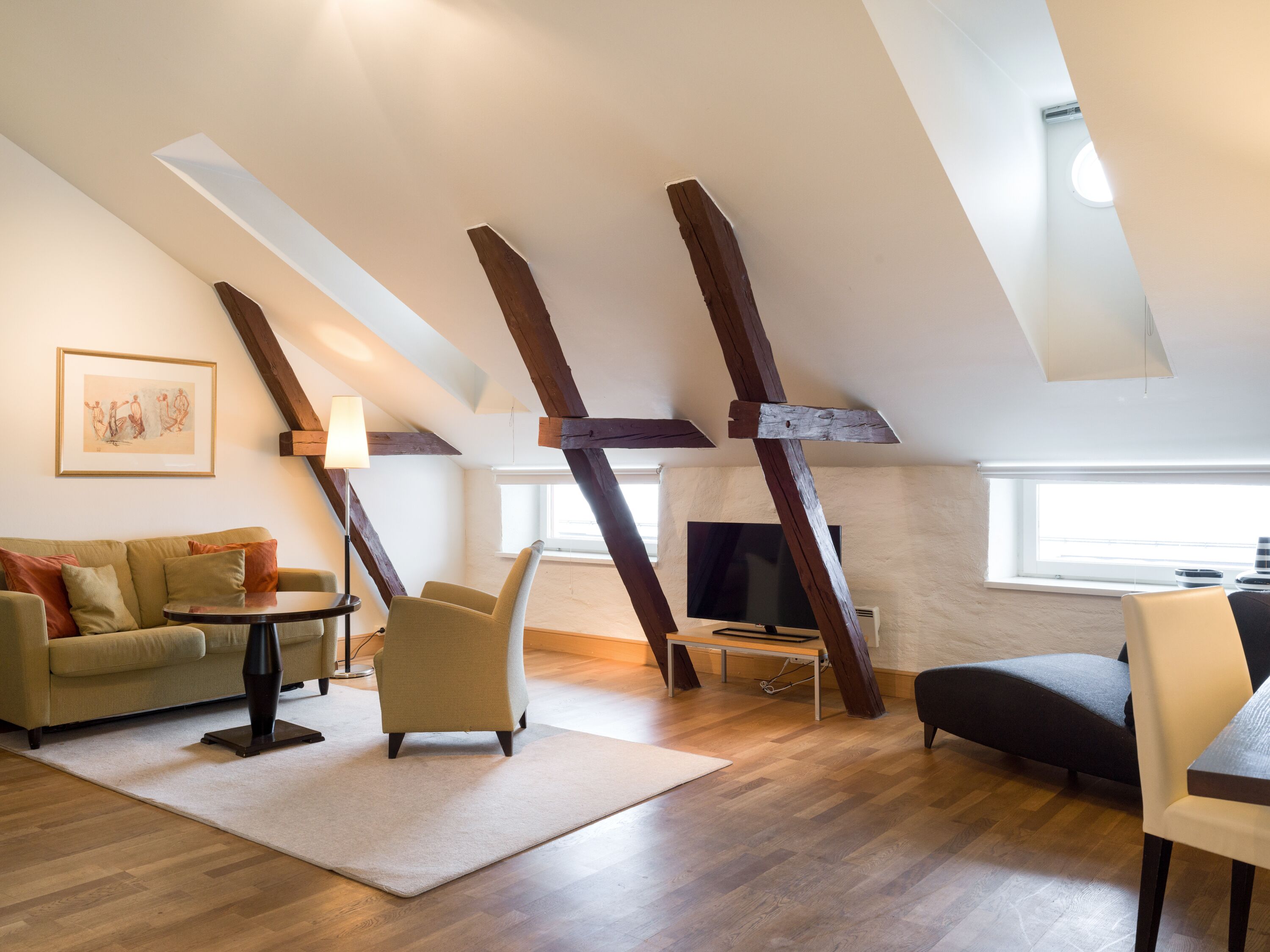Una sala de estar estilo loft con vigas de madera a la vista, un sofá, sillones, una mesa de centro y un televisor de pantalla plana.