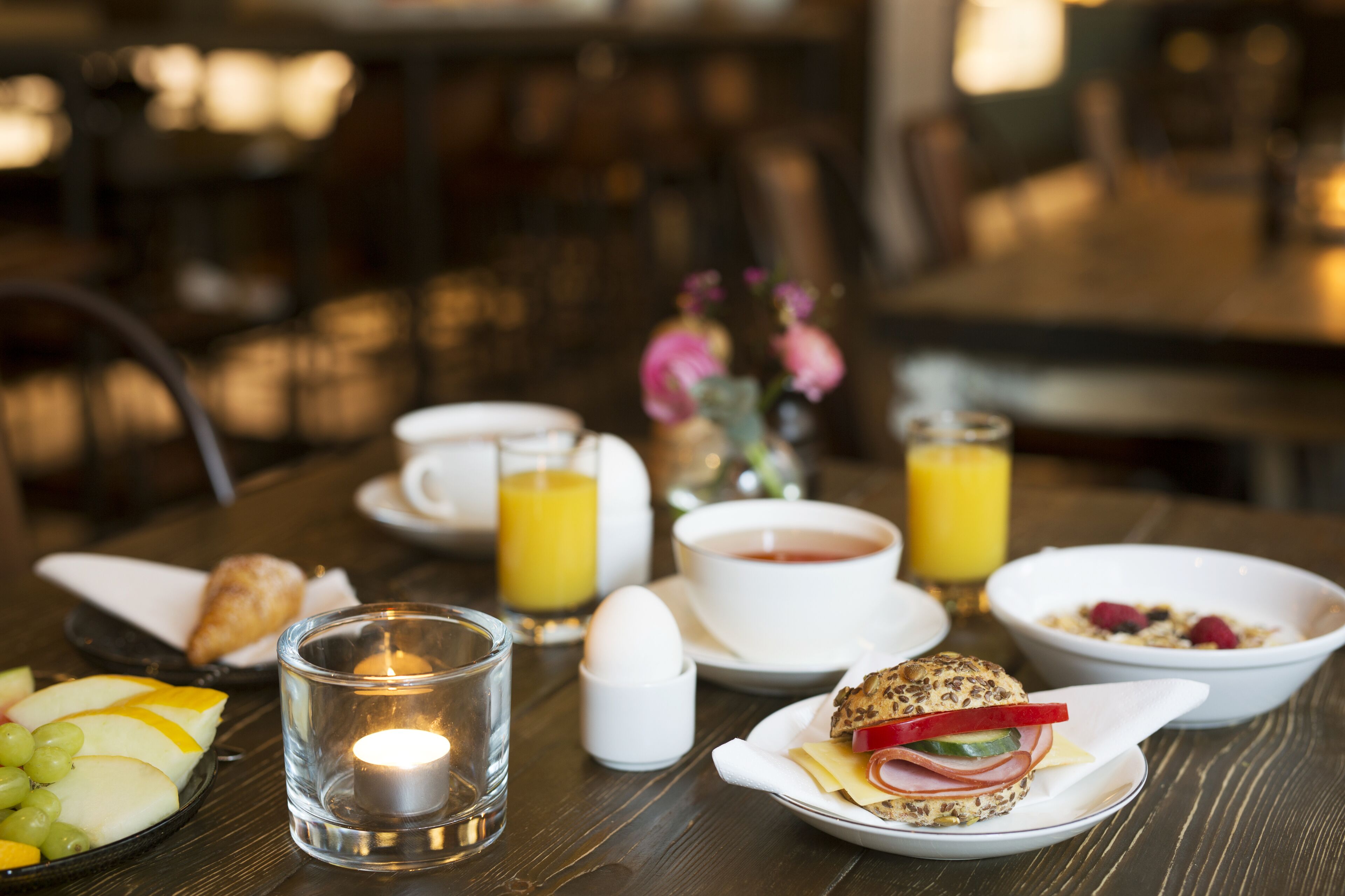 A breakfast table with various food items, including eggs, toast, and fruit, along with cups of tea and orange juice.