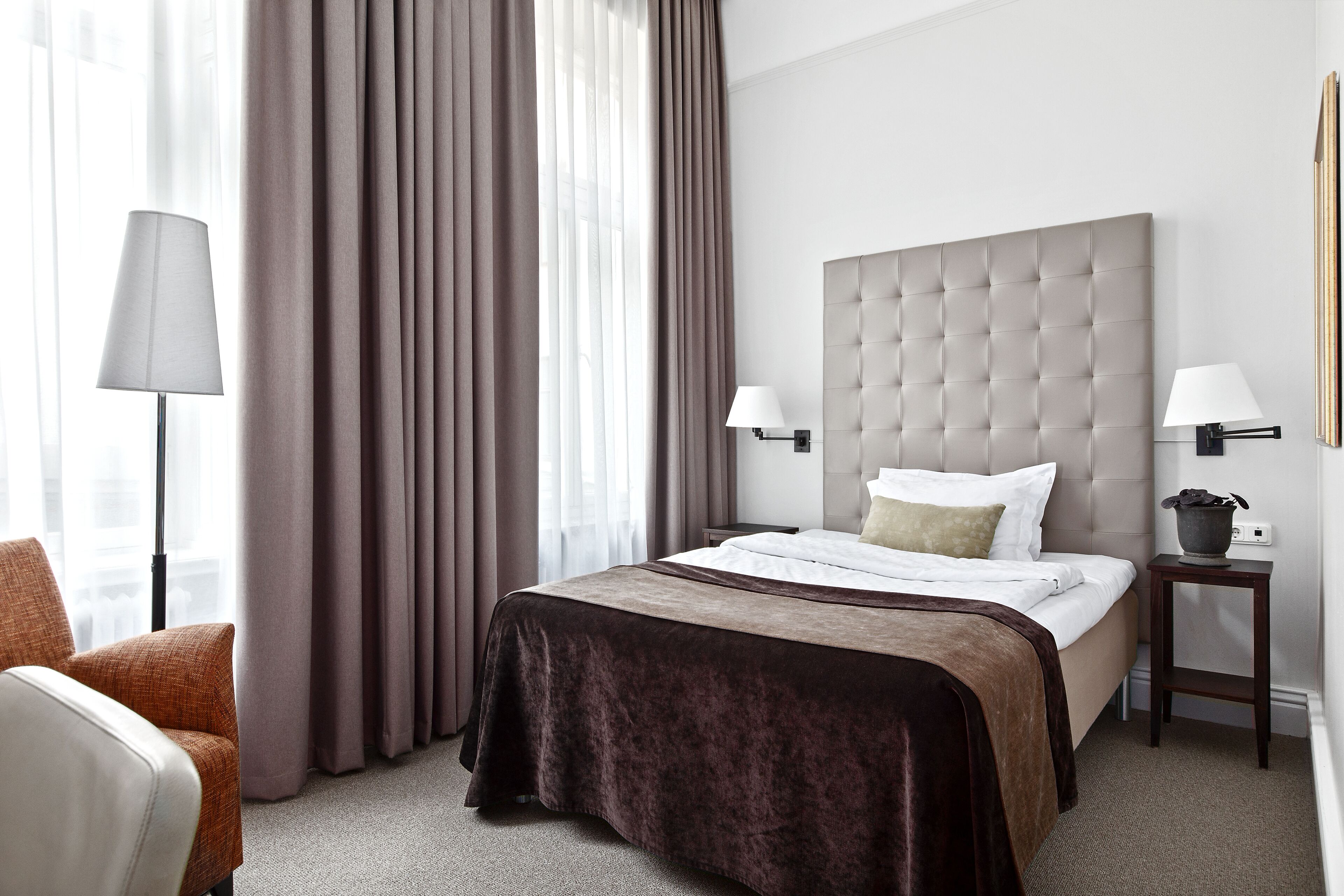 A hotel room with a large bed, two bedside lamps, a nightstand, and a chair.