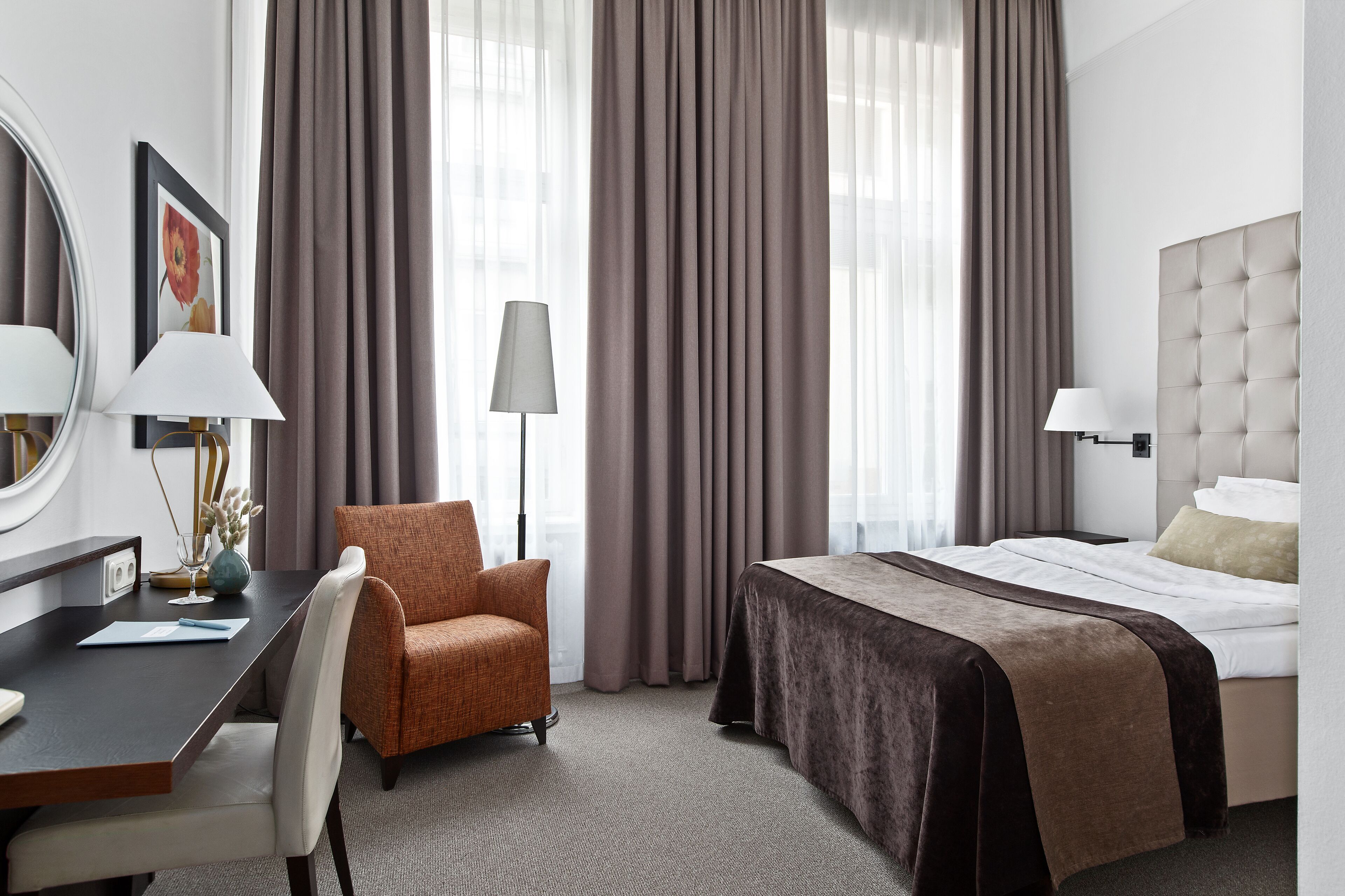 A hotel room with a bed, a desk, a chair, and a lamp.