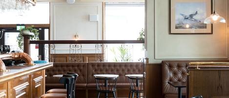 Un restaurante con zona de bar, disposición de mesas y un cuadro en la pared.