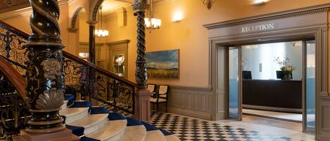 A grand staircase with ornate balustrades leading to a reception area with a checkered floor.