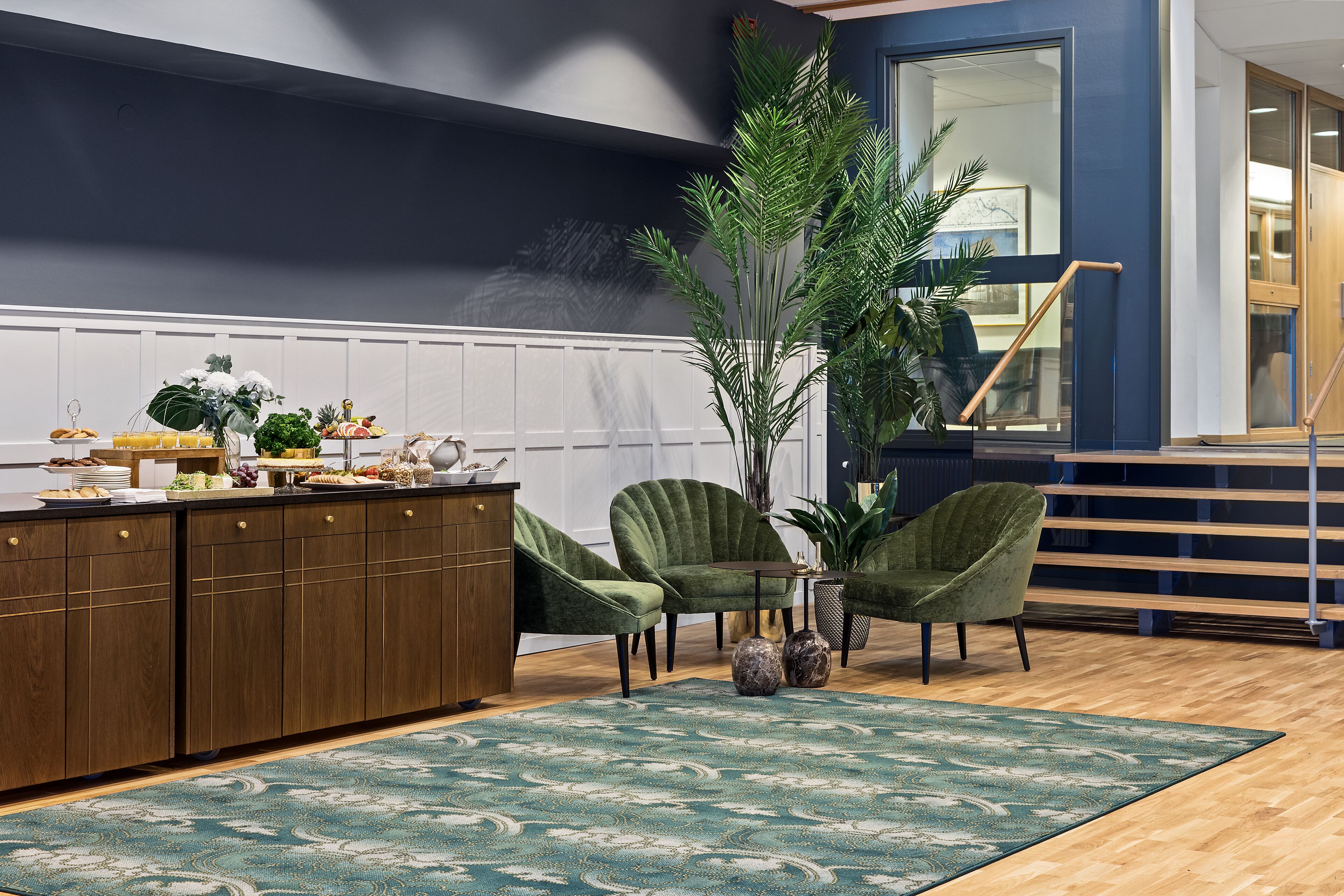 Una sala de estar moderna con un aparador de madera, dos sillones verdes, una mesa de centro y una planta grande.