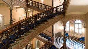Eine prächtige Treppe mit aufwendiger Metallgeländerung und blauen, gepolsterten Stufen, die zu einem Schachbrettmuster-Bodenbereich mit Sitzgelegenheiten führt.