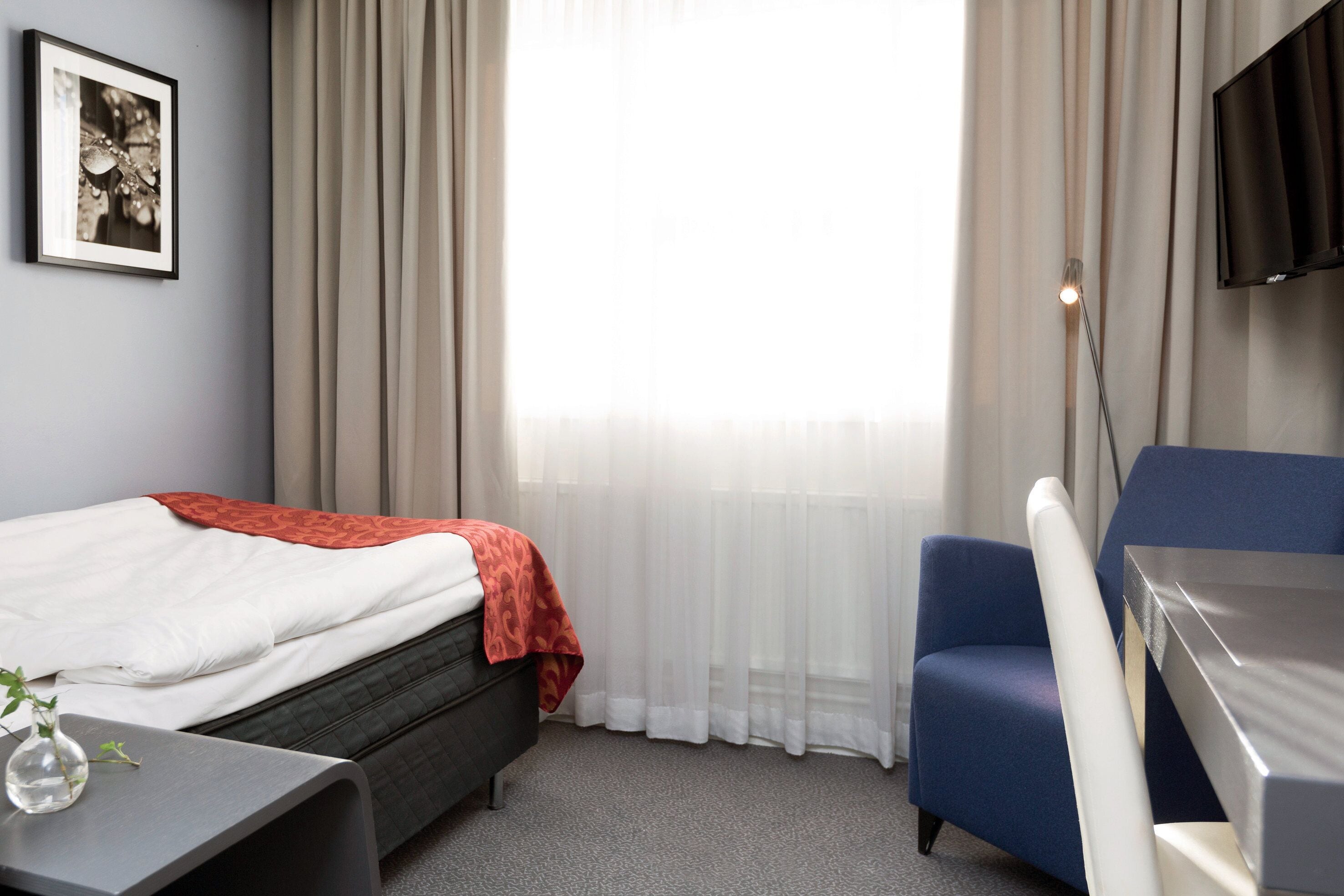 A hotel room with a bed, a desk, a chair, a TV, and a window with curtains.
