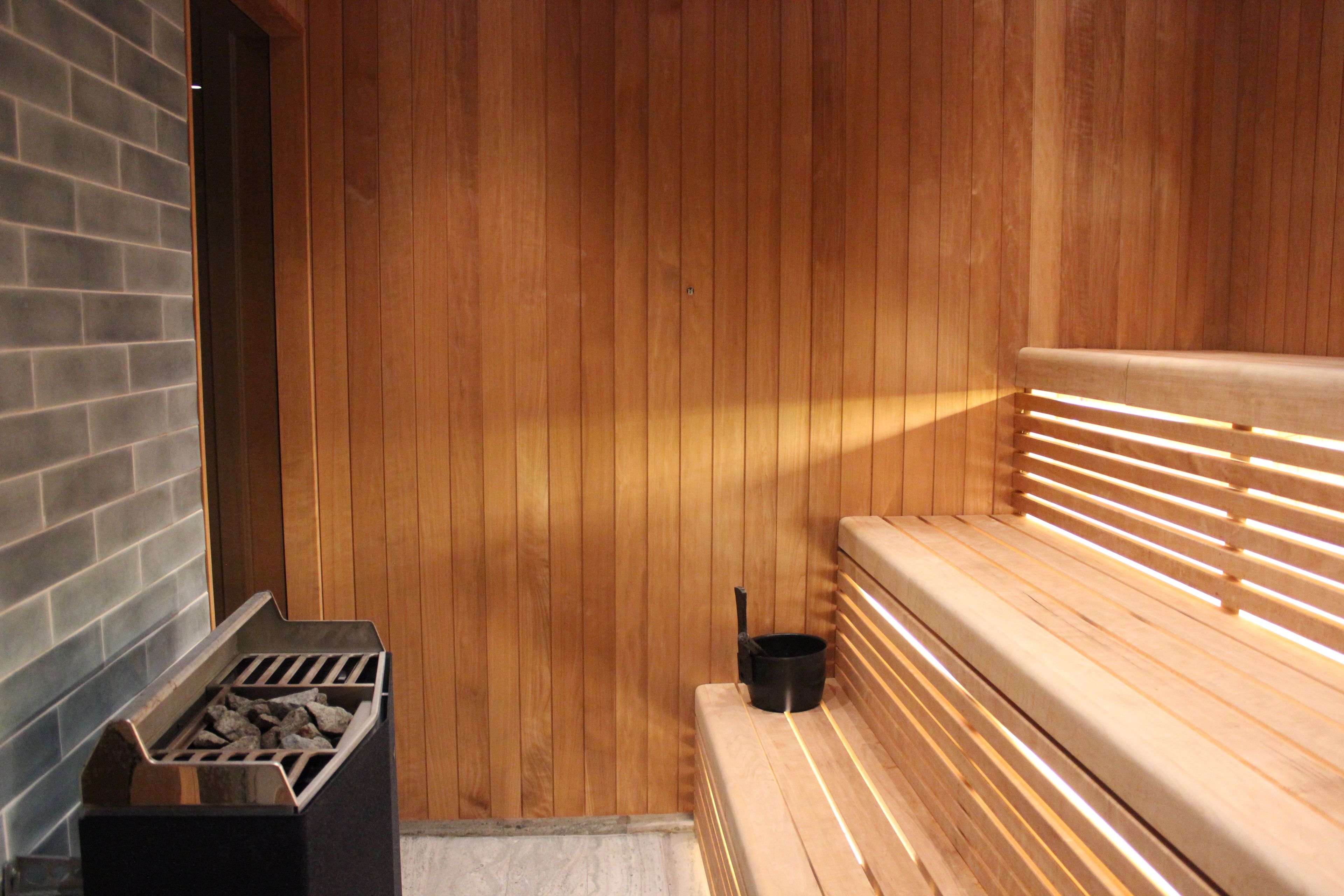 A sauna with wooden walls and benches, a brick wall on one side, and a metal container with rocks.