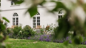 Un edificio con tres ventanas arqueadas y un jardín con flores moradas y una mesa de madera.
