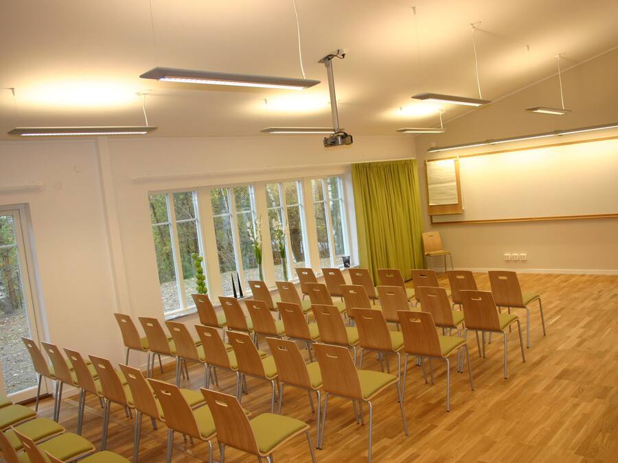 A conference room with rows of chairs, large windows, and a projector screen.