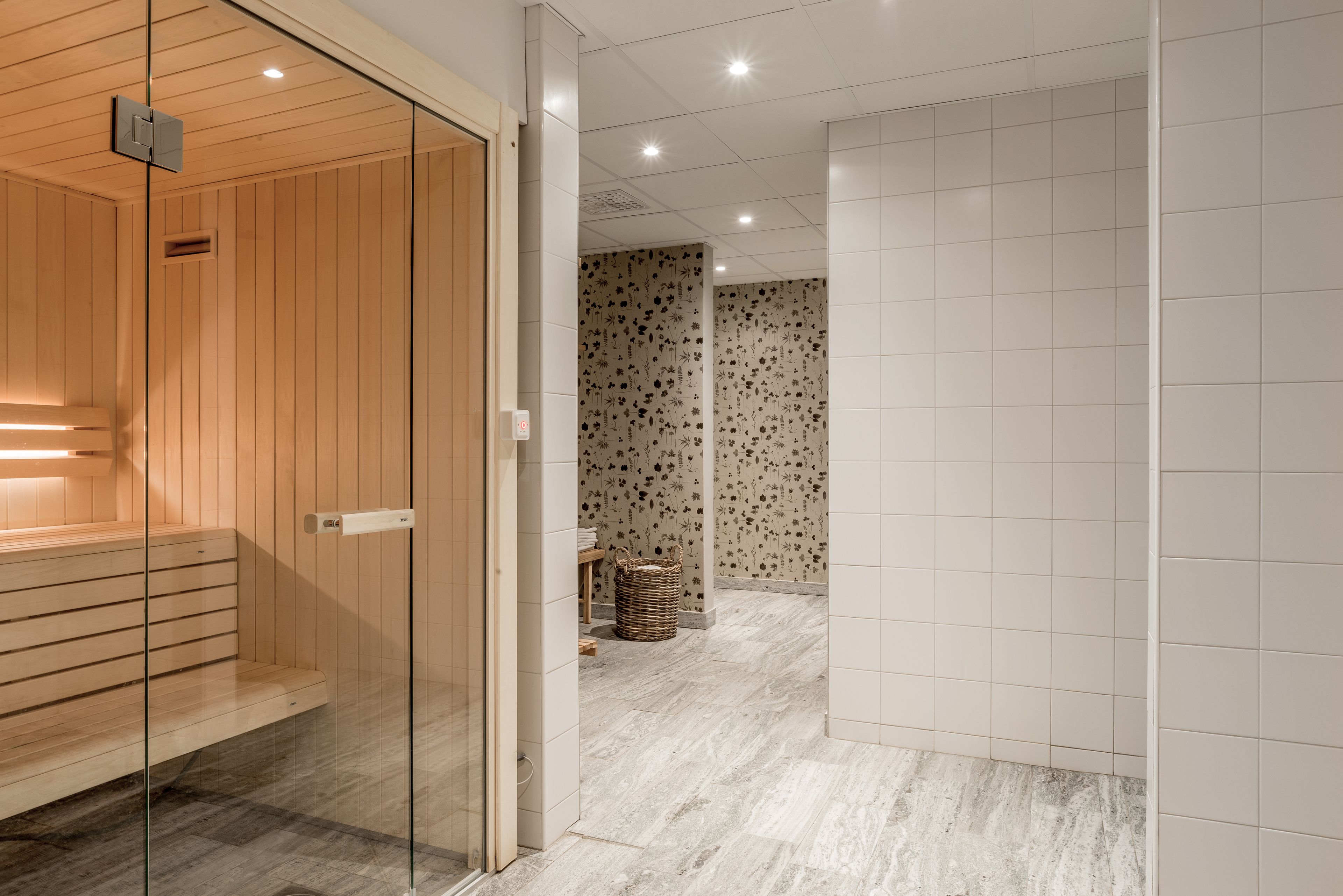 Ein moderner Wellnessbereich mit Holzbiosauna, Glastrennwand und einer Wand mit Musterung.