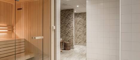 Ein moderner Wellnessbereich mit Holzbiosauna, Glastrennwand und einer Wand mit Musterung.