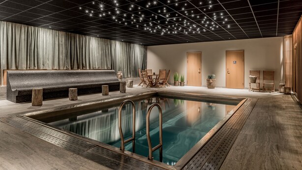 Un área de piscina interior moderna con una piscina cristalina, un deck de madera y un techo con luces que simulan estrellas.