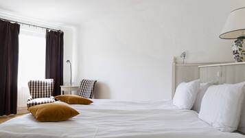 Un dormitorio con una cama grande, dos almohadas, una silla, una mesita y una lámpara.