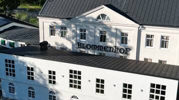 Een groot wit gebouw met de naam “Hotel Blommenhof” op de gevel, met meerdere ramen en een schuin dak.