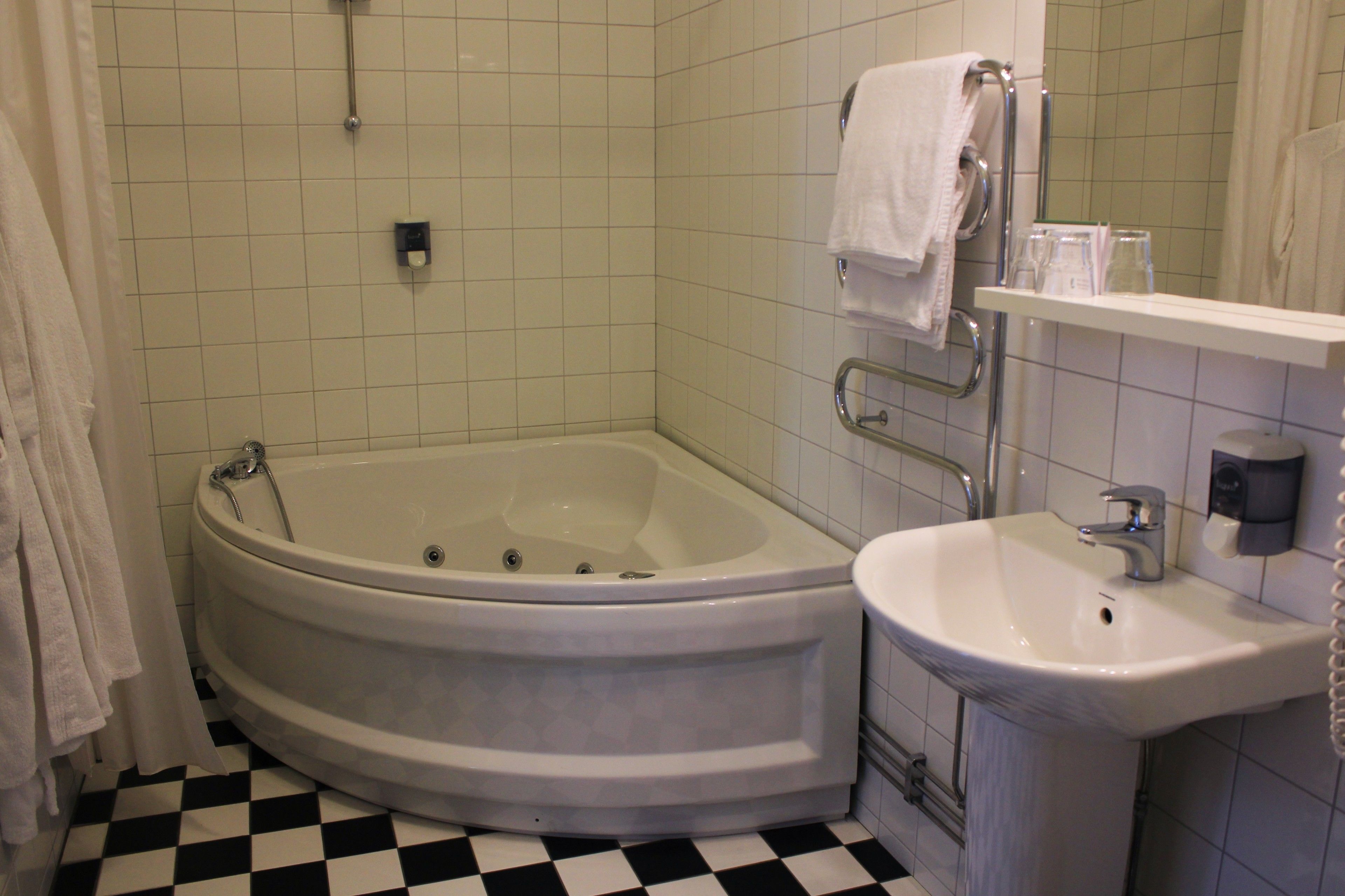 Un baño con una bañera blanca, un lavamanos y un espejo. Hay un perchero sobre el lavamanos y una estantería con artículos de aseo.
