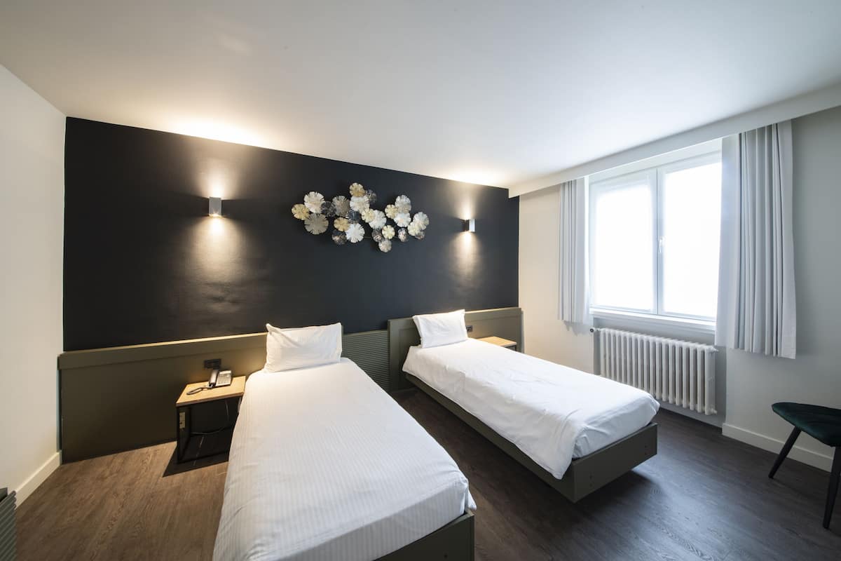 A hotel room with two single beds, a dark accent wall, a decorative wall piece, a bedside table with a phone, and a window with curtains.