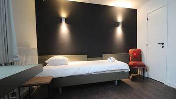 Una habitación de hotel moderna con cama, mesita de noche, silla y dos luces fijadas a la pared.